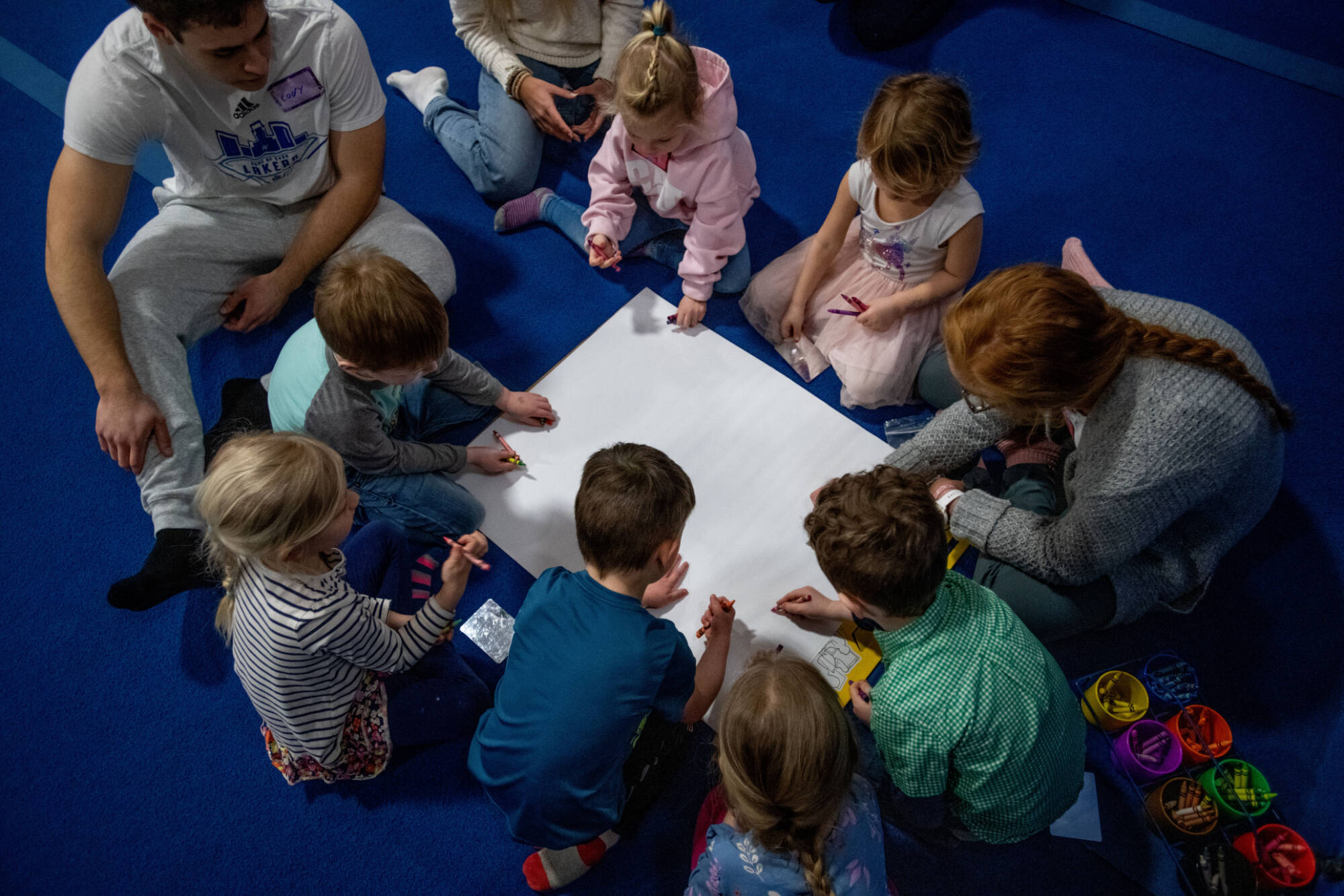 group of children receiving physical education instruction from two aduls. photo is from above view looking down